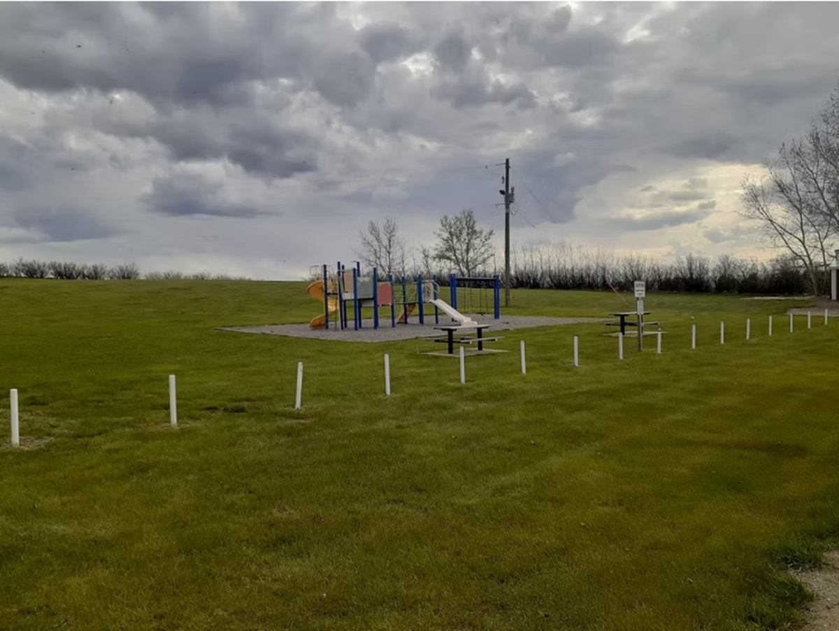 Playground with slides and swings in open grassy field under cloudy sky.