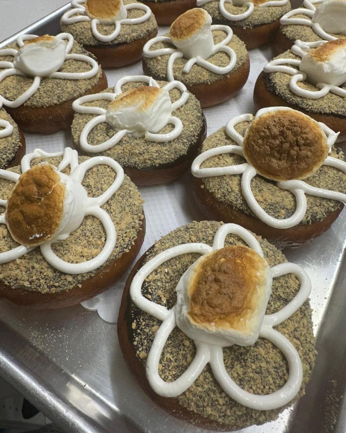 Baked pastries with white icing piping, sprinkled with crumb topping on a metal tray.