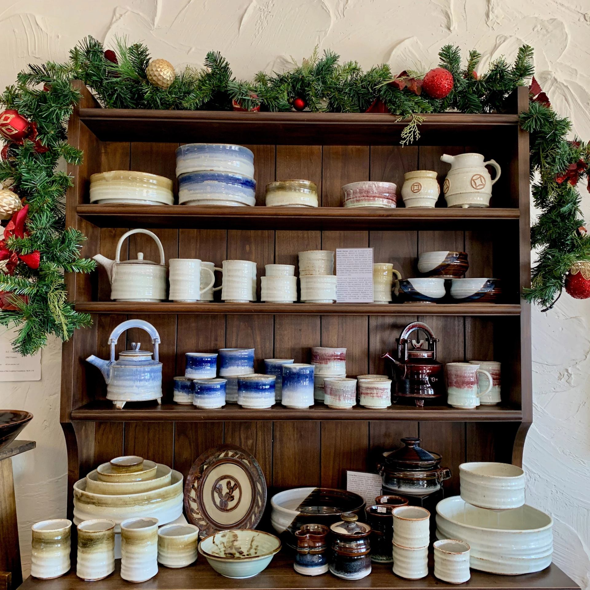 Ceramic mugs, bowls, and teapots on festive shelves with garland and ornaments.