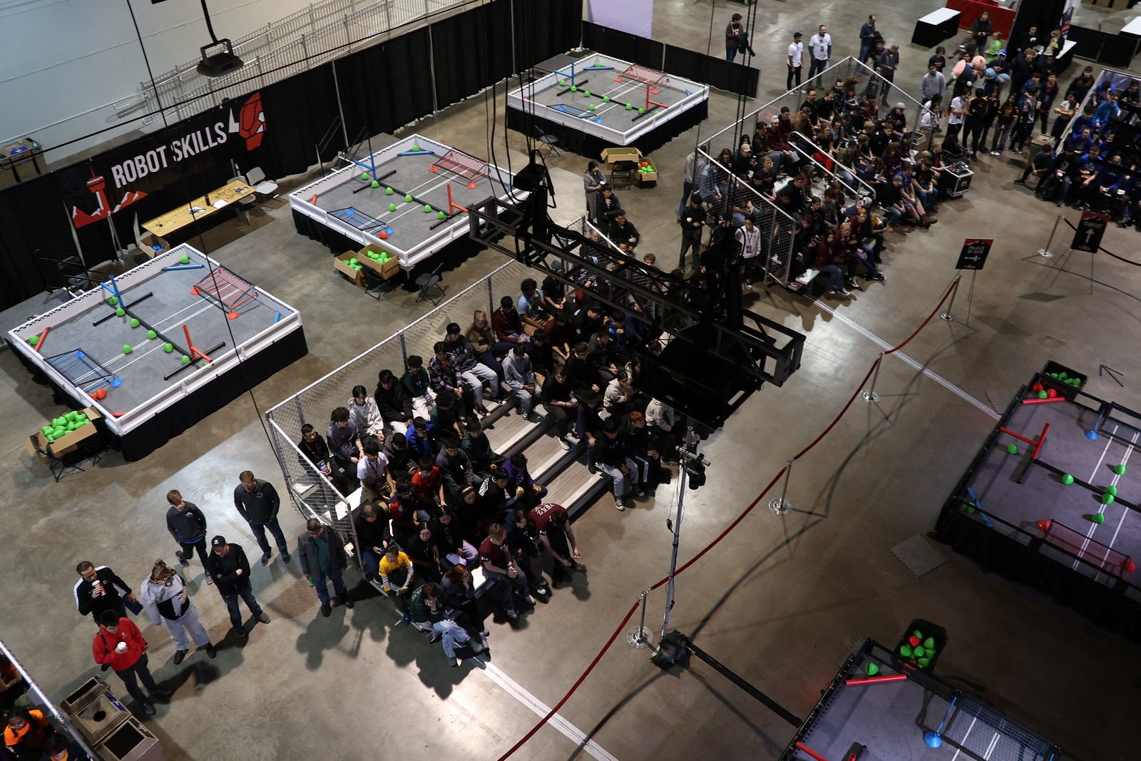 Robotics tournament with multiple competition fields and audience seating in a large venue.