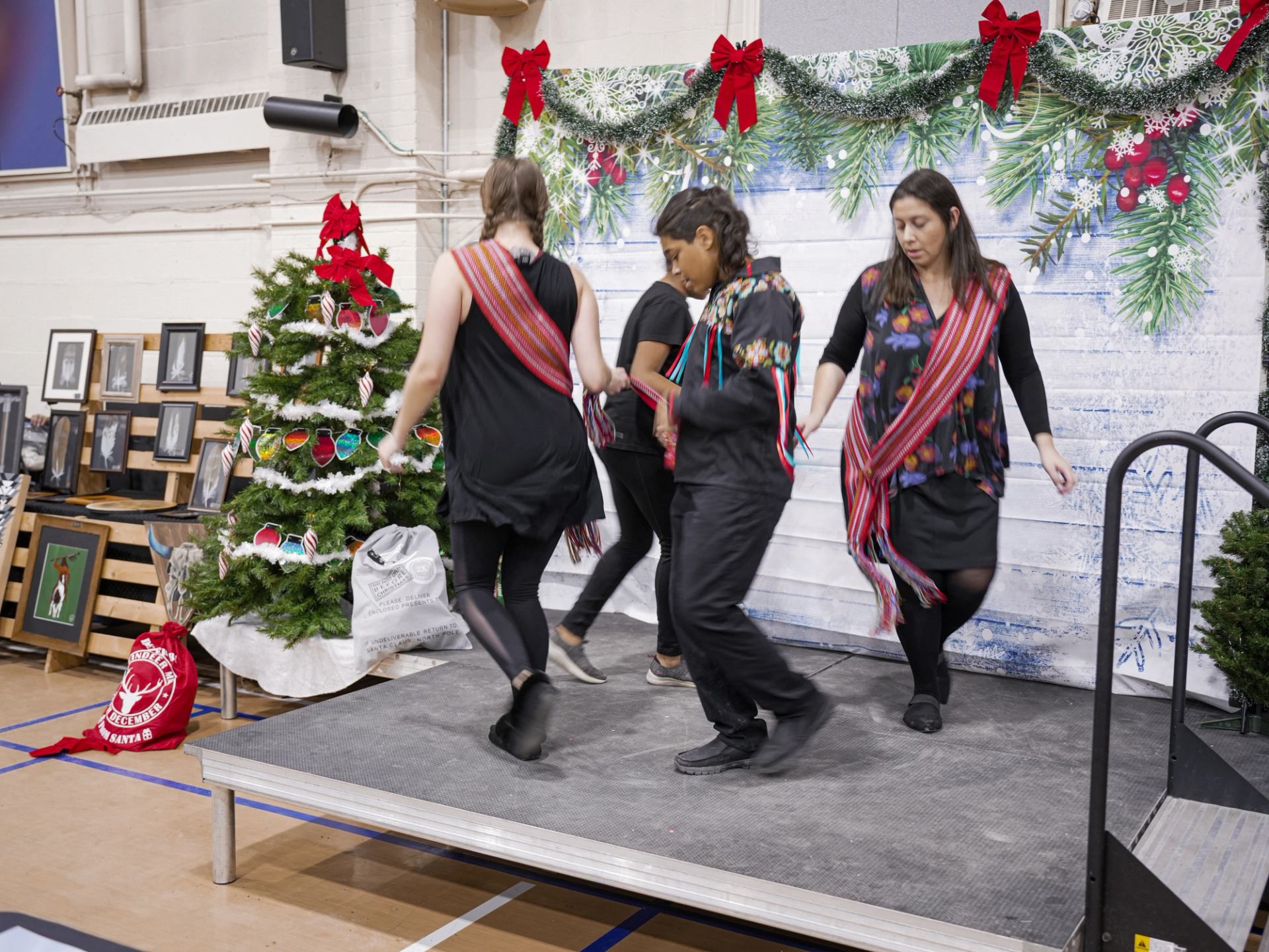  Four performers in sashes dance on a festive stage with holiday decorations.