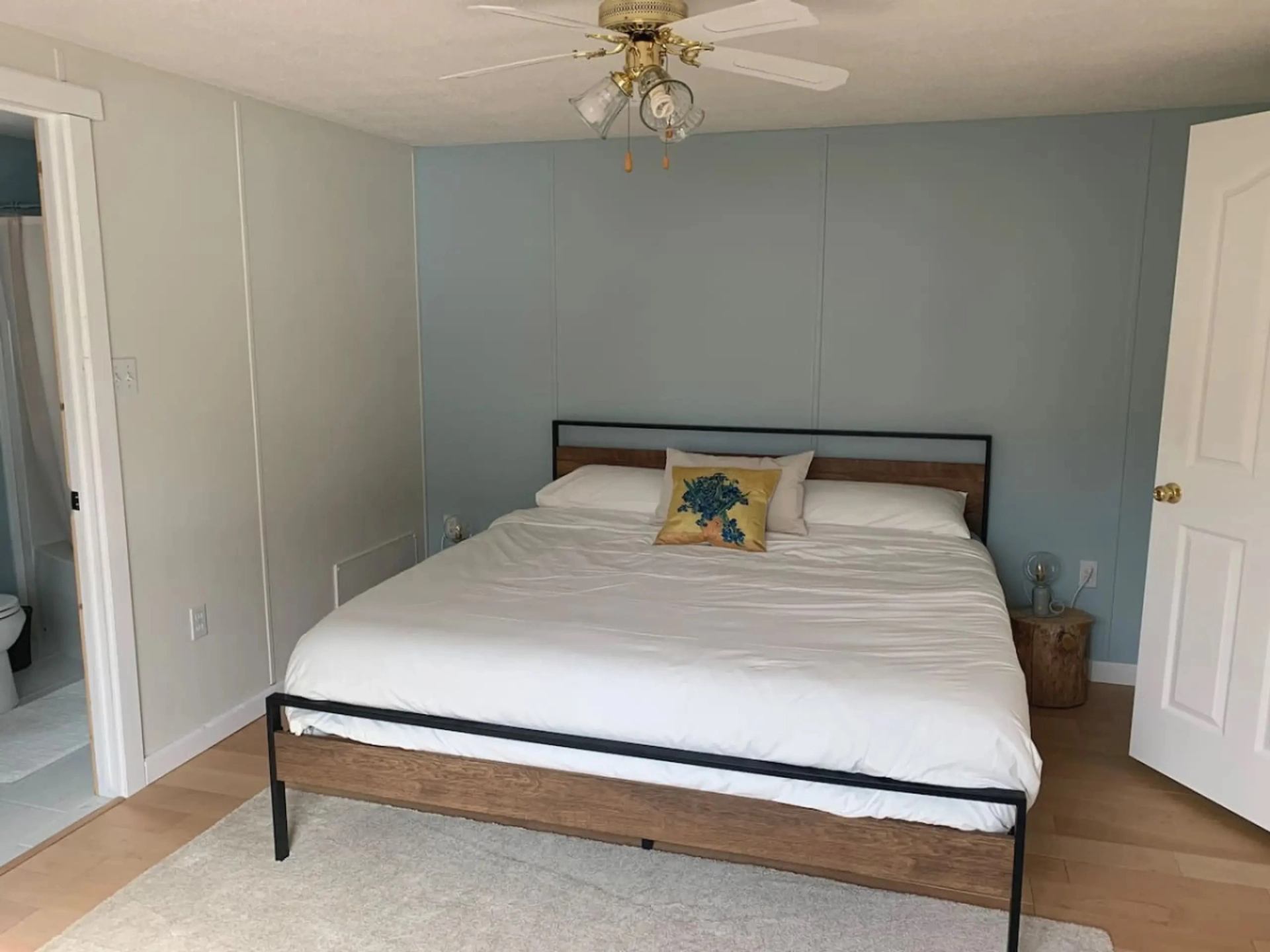 Bedroom with white bed, blue accent wall, ceiling fan, and open bathroom doorway.
