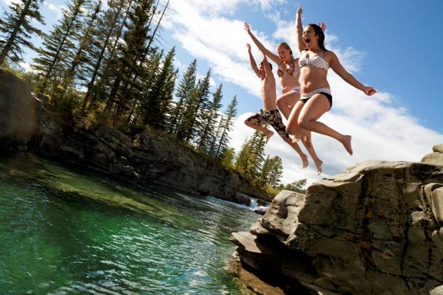 Three teenagers jumping off a cliff into water at Castle Falls, near Pincher Creek in Southern Alberta.