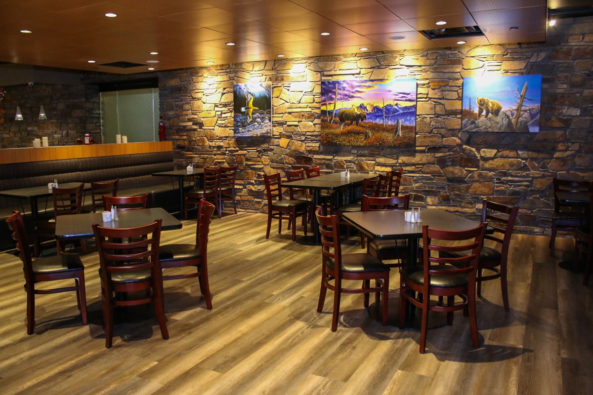Cozy dining room with wooden tables, stone wall, and nature-themed paintings.
