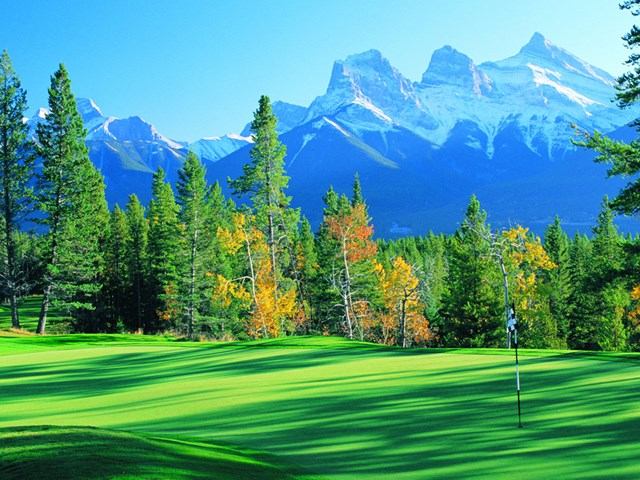 Lush golf course with vibrant trees and majestic Rocky Mountains in the background.