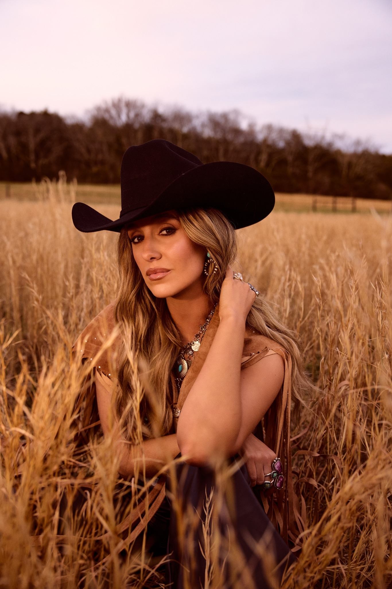 Seated Lainey Wilson in field wearing black hat and jewelry.
