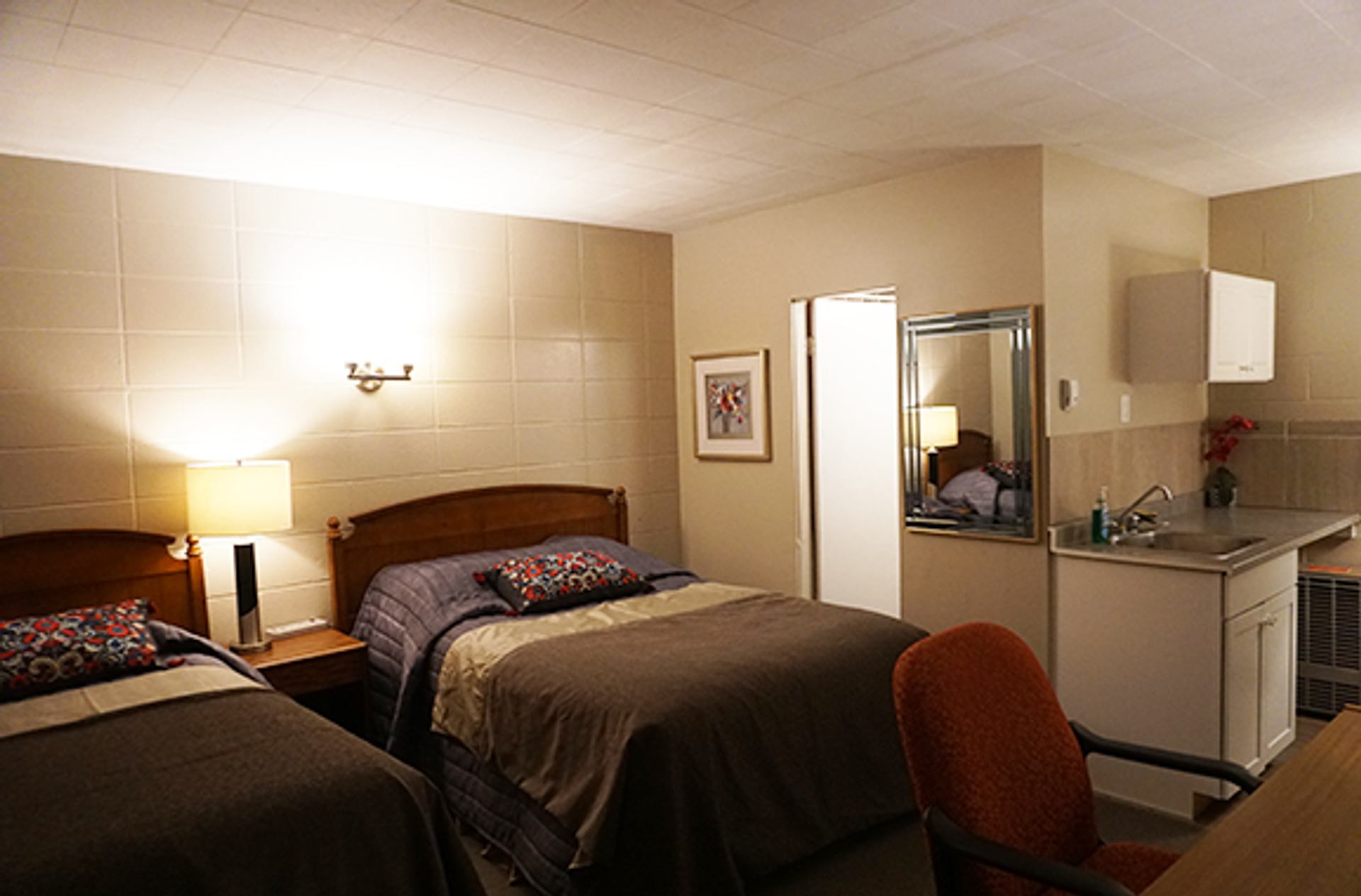 Motel room with two beds, small kitchen area, desk, and mirror.
