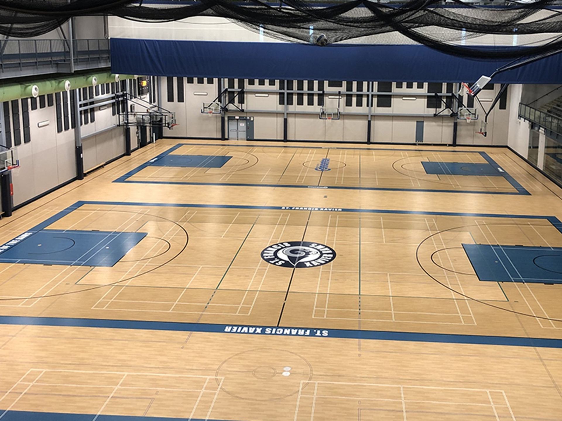 Empty indoor gymnasium with multiple basketball courts and St. Francis Xavier logo at centre.