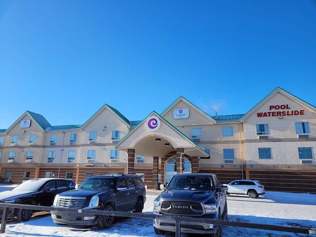 Exterior view of Coast Grimshaw Hotel & Suites with parked cars and clear blue sky.