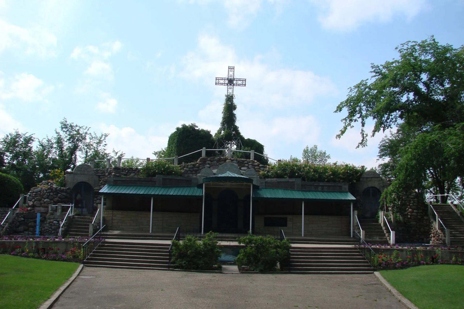 Stone grotto with stairs, greenery, and a cross above at the museum grounds.
