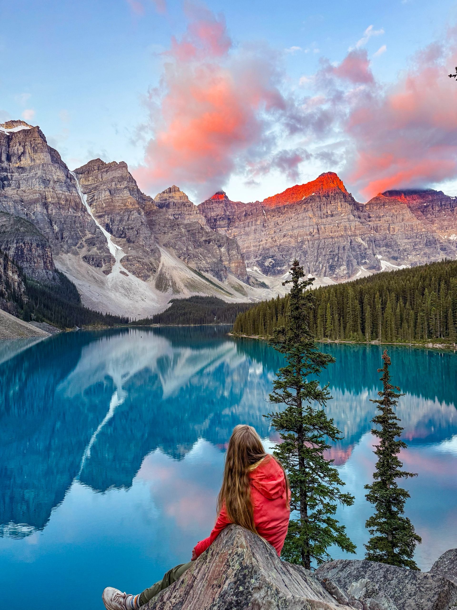 Person sitting on rock watching sunrise over Moraine Lake’s peaks.
