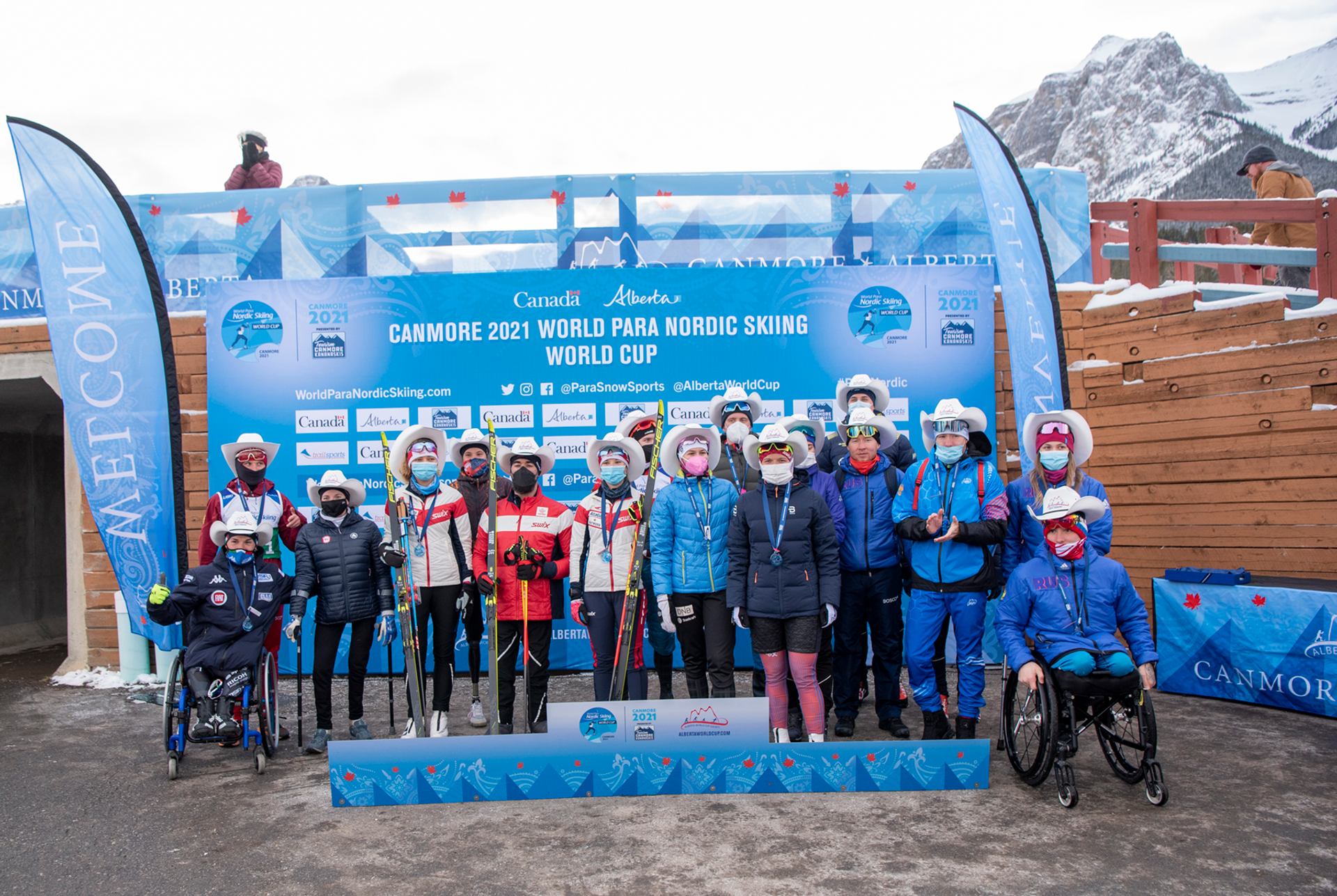 Para Nordic skiers and staff pose with medals and cowboy hats at Canmore 2021 World Cup podium.