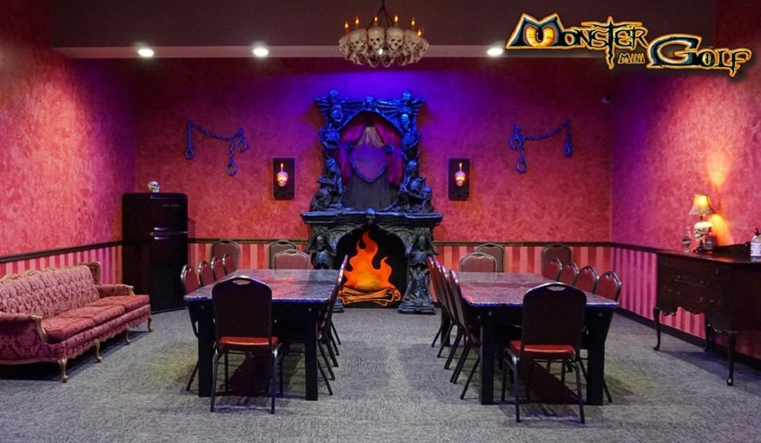 Party room with tables and chairs, faux fireplace, Monster Mini Golf logo on wall.