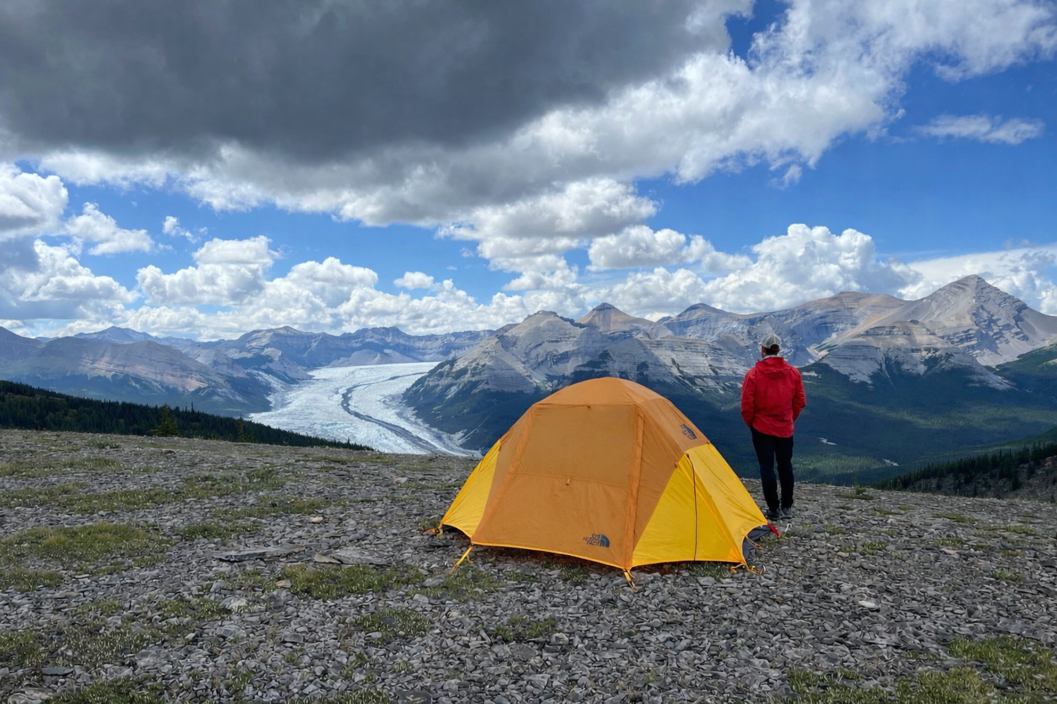 Bright tent pitched on ridge with glacier and mountains beyond