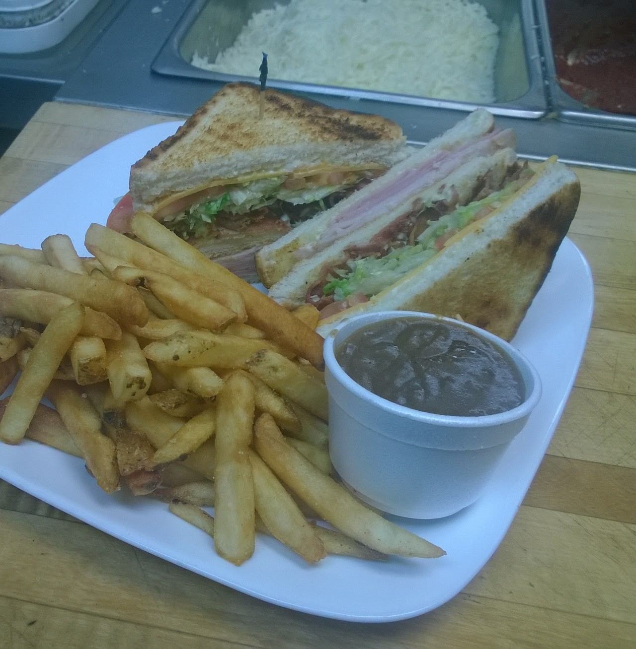 Plate with club sandwich, golden fries, and a cup of brown gravy on a wooden surface.