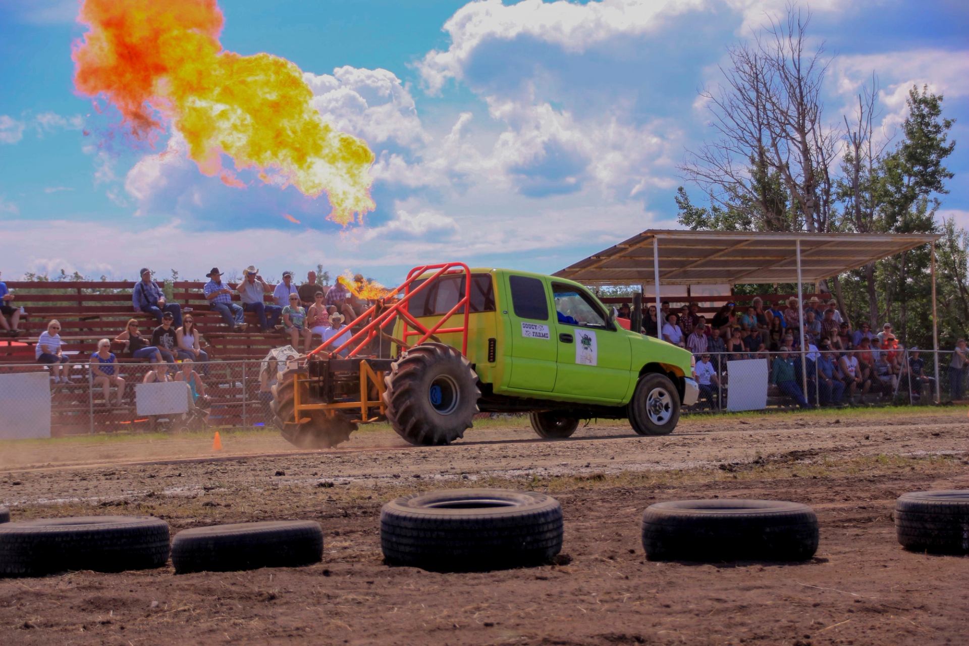 Monster truck shooting flames from the back while driving on a dirt track with spectators watching.