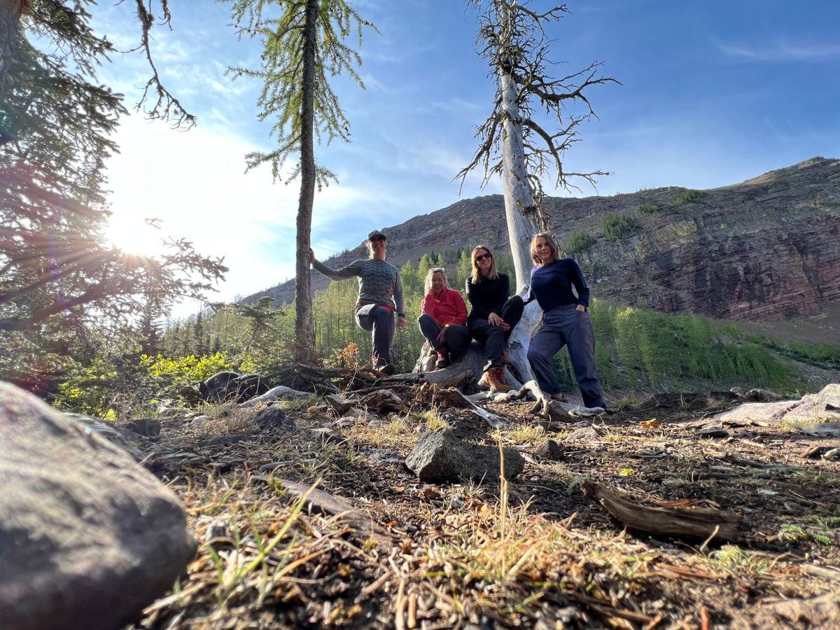 Four people pose on rocky ground among tall trees with a forested mountain backdrop.