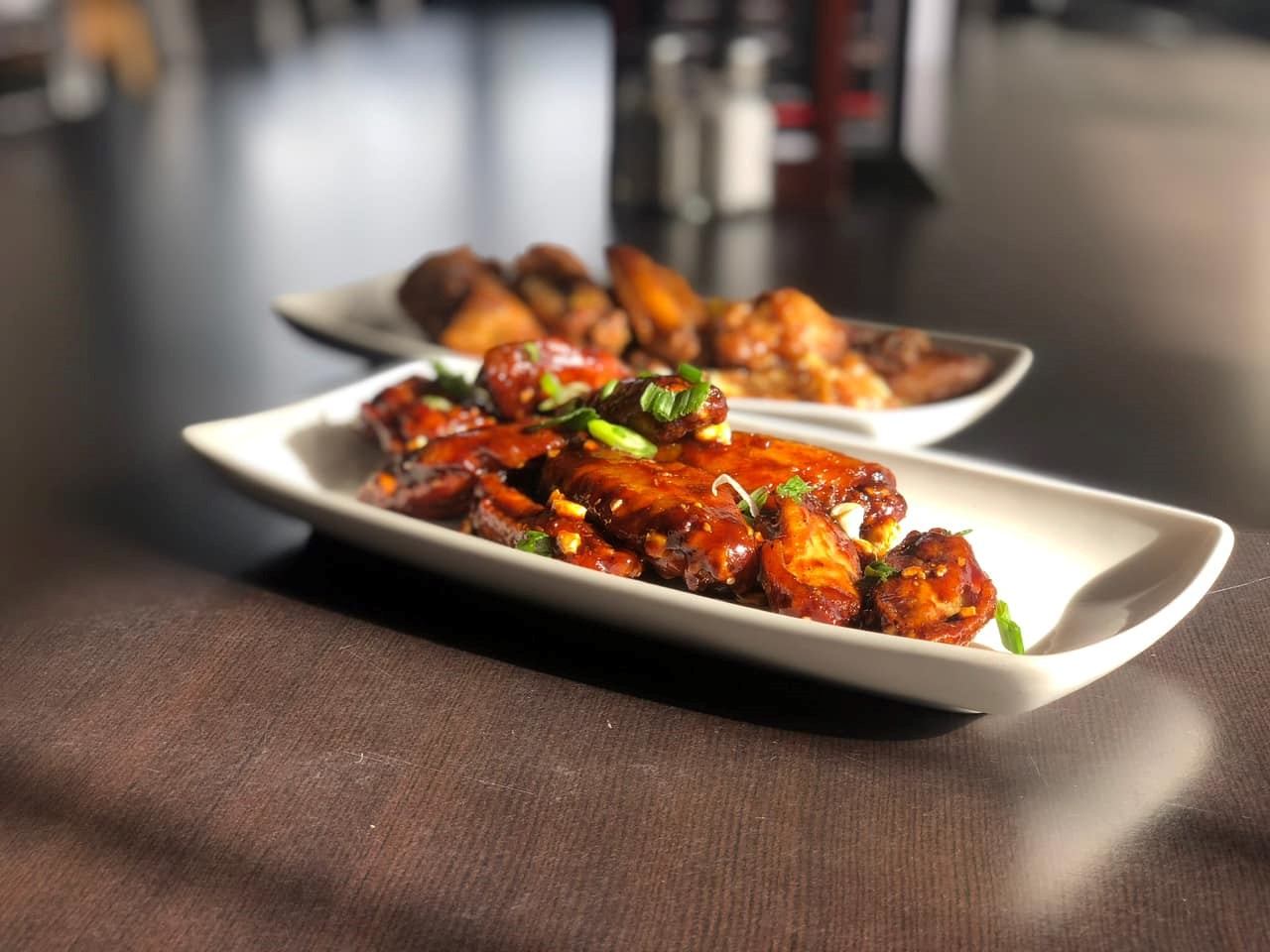Glazed chicken wings and roasted potatoes on white plates in restaurant setting.