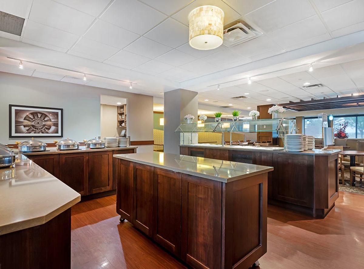 Hotel buffet area with wooden counters, covered serving dishes, plates and decorative plants.