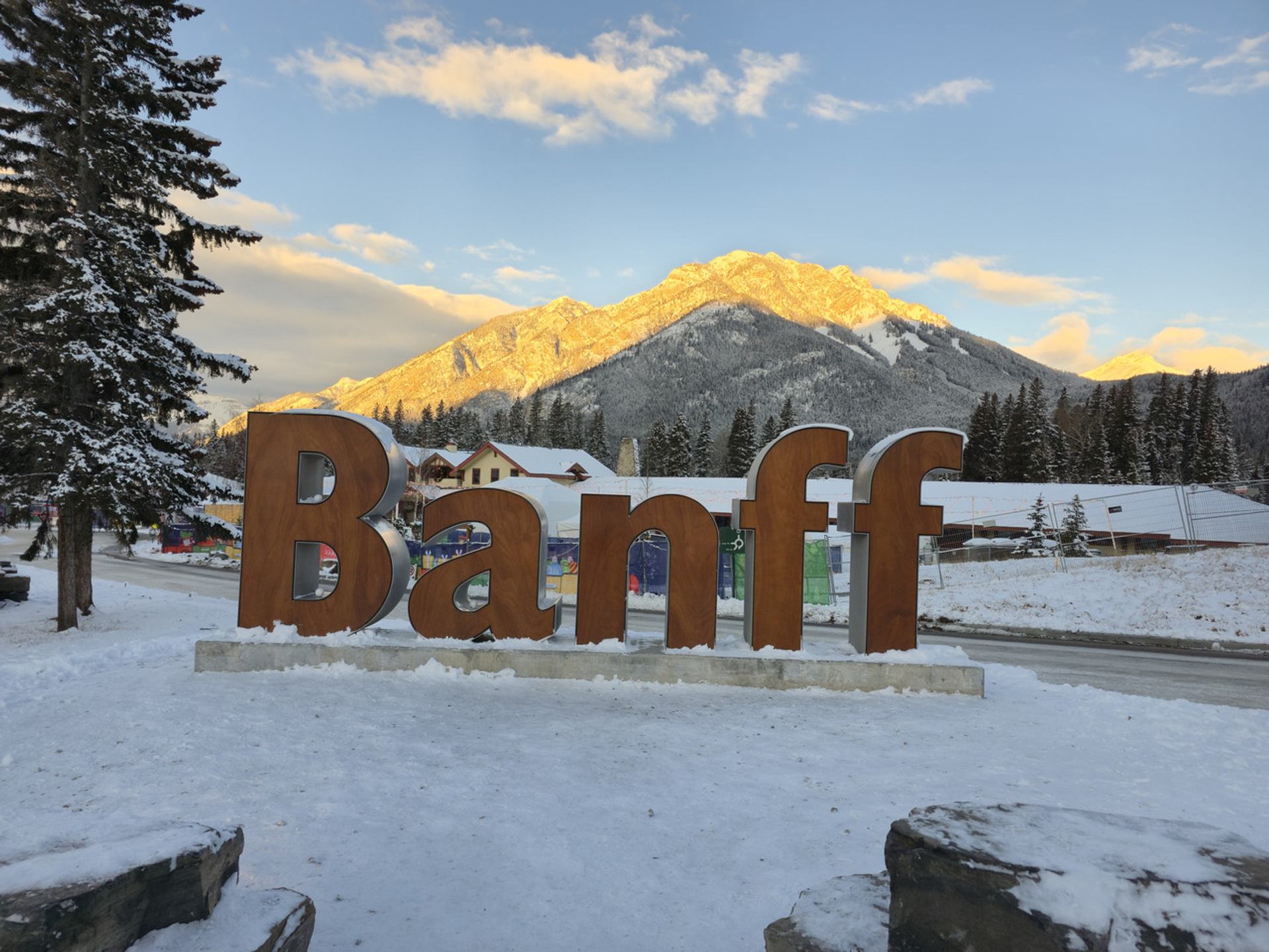 Large "Banff" sign in a snowy landscape with a sunlit mountain in the background.