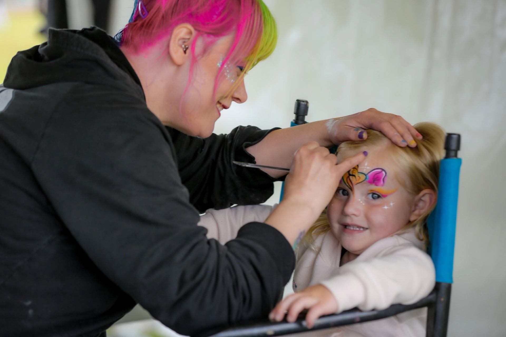 Artist painting a child's face at a festival booth.