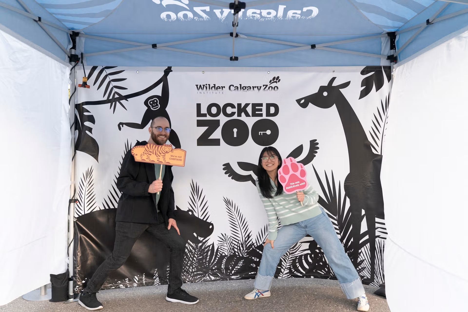 Two people pose with animal props under a Calgary Zoo Locked Zoo banner.