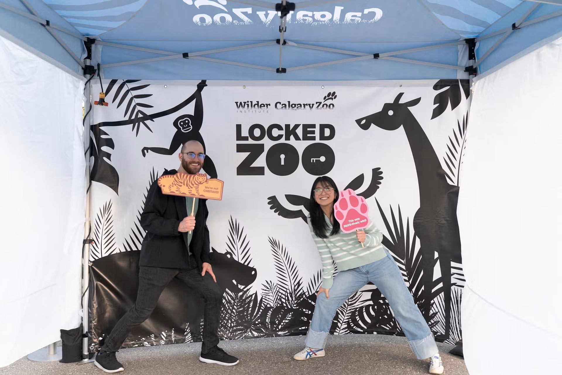 Two people pose with animal props under a Calgary Zoo Locked Zoo banner.