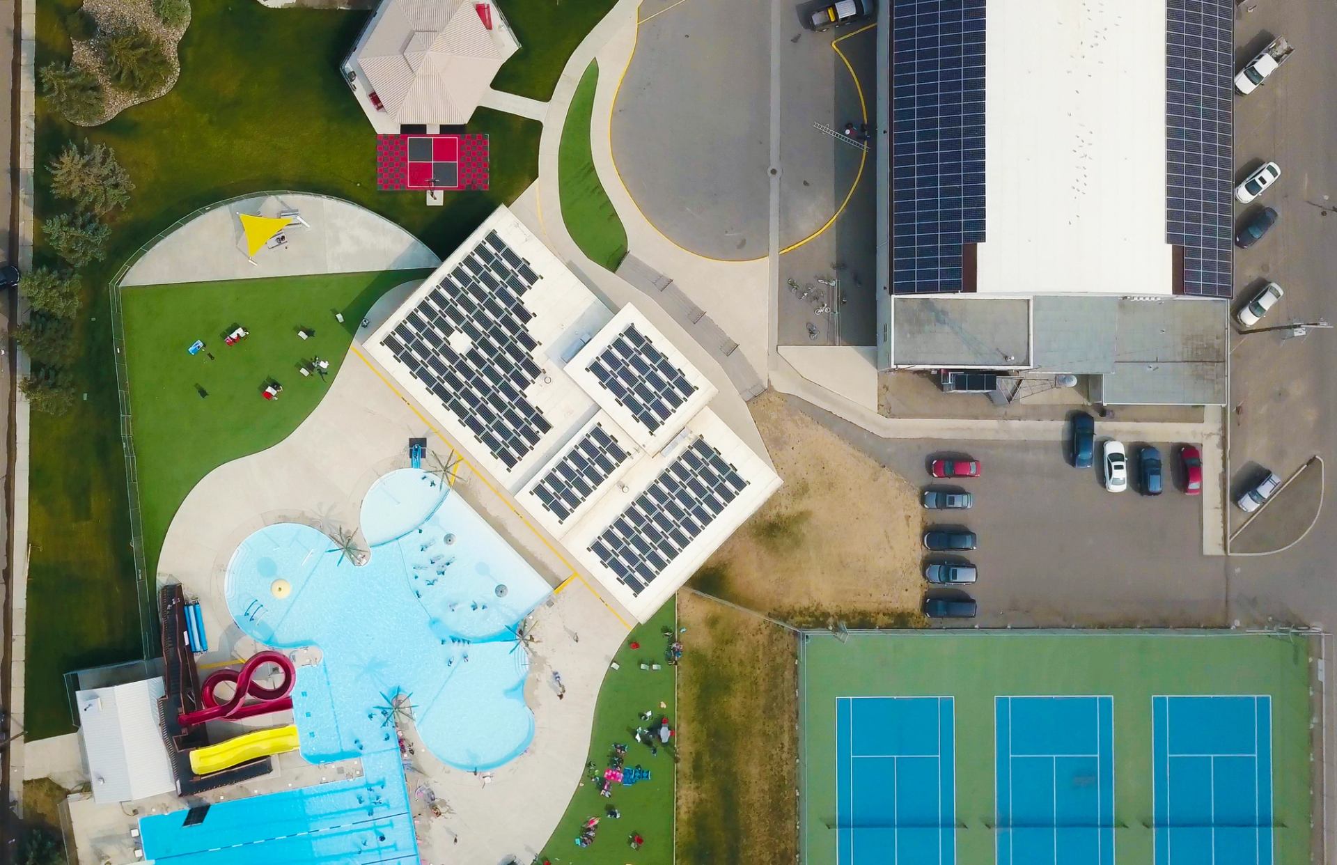 Aerial view of pools, slides, tennis courts, and solar-roofed building at Centennial Park.