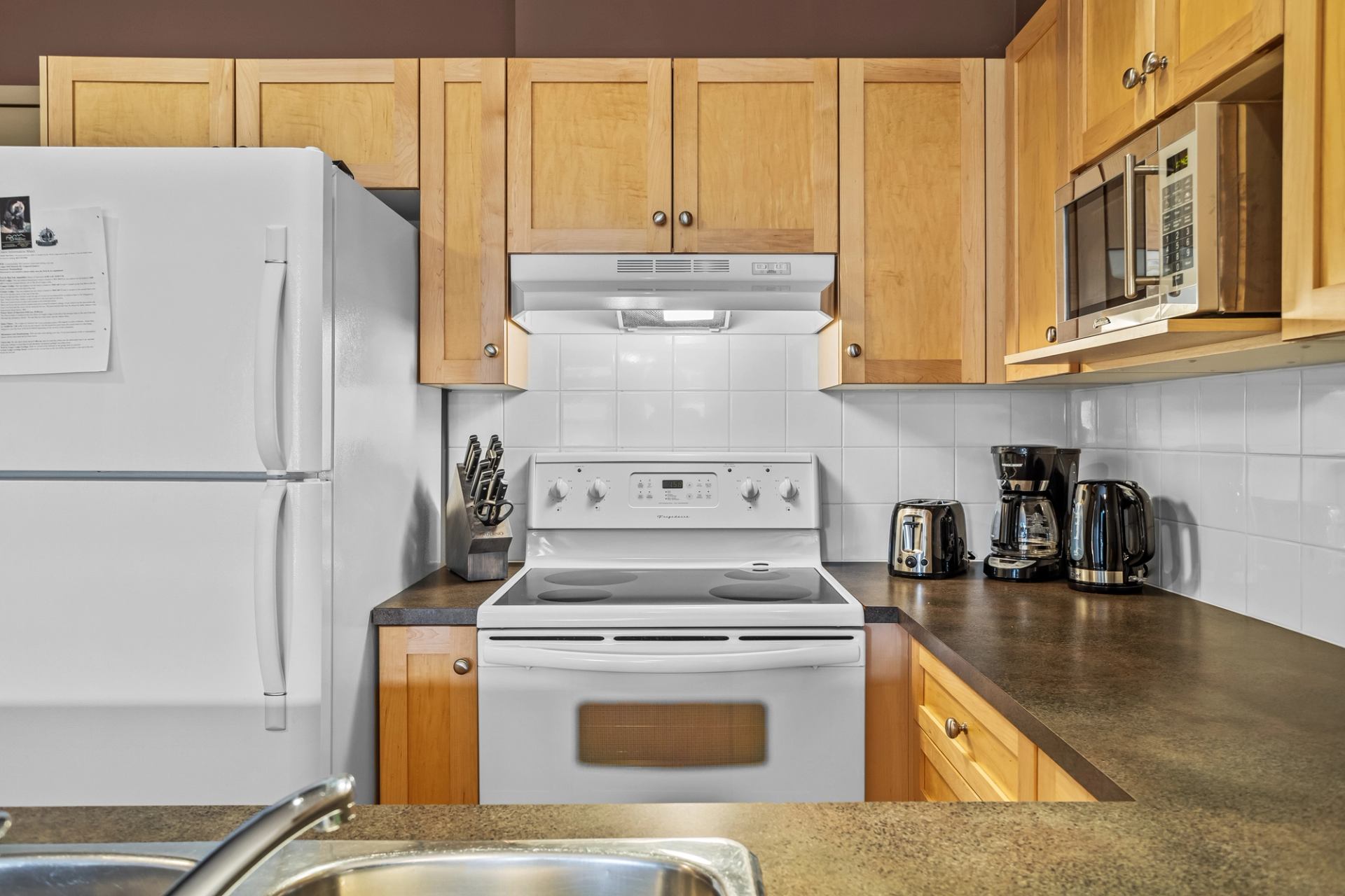 Kitchen with wood cabinets, white appliances, tiled backsplash and countertop coffee makers.