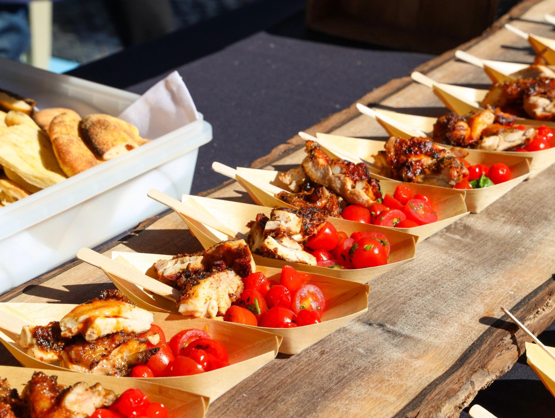 Wooden trays of grilled chicken and cherry tomatoes arranged on a rustic wooden table.
