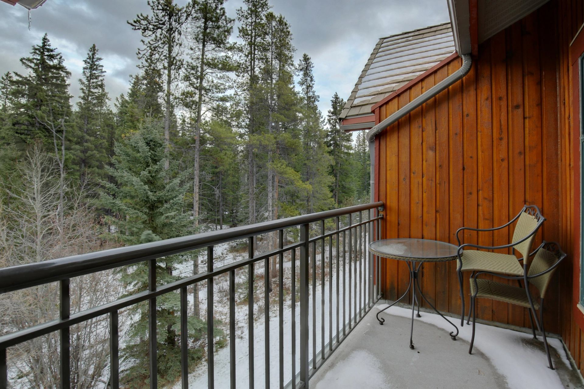 Small balcony with table and chairs overlooking a forest of tall trees.