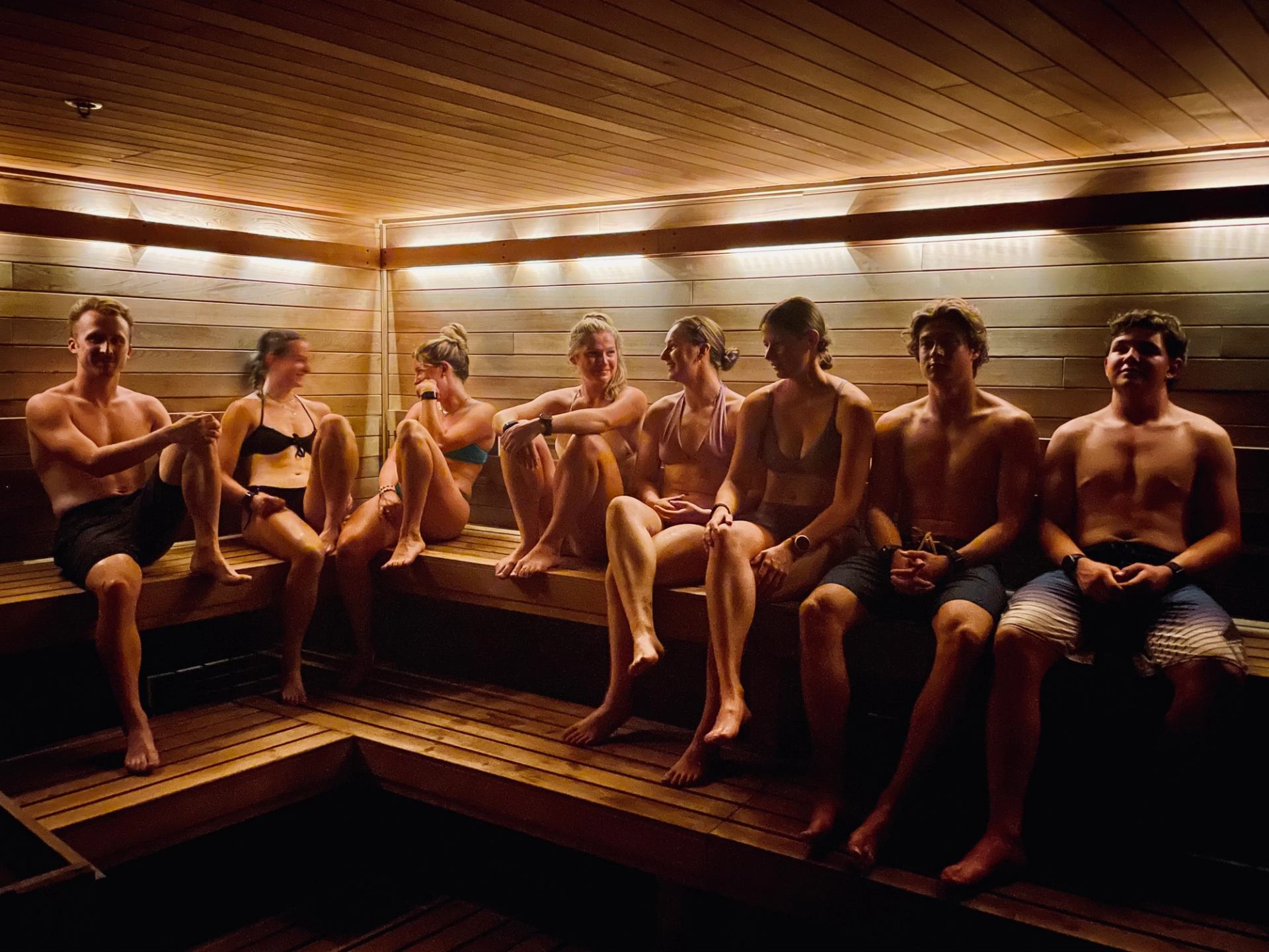 Group of people relaxing inside a warmly lit wooden sauna.