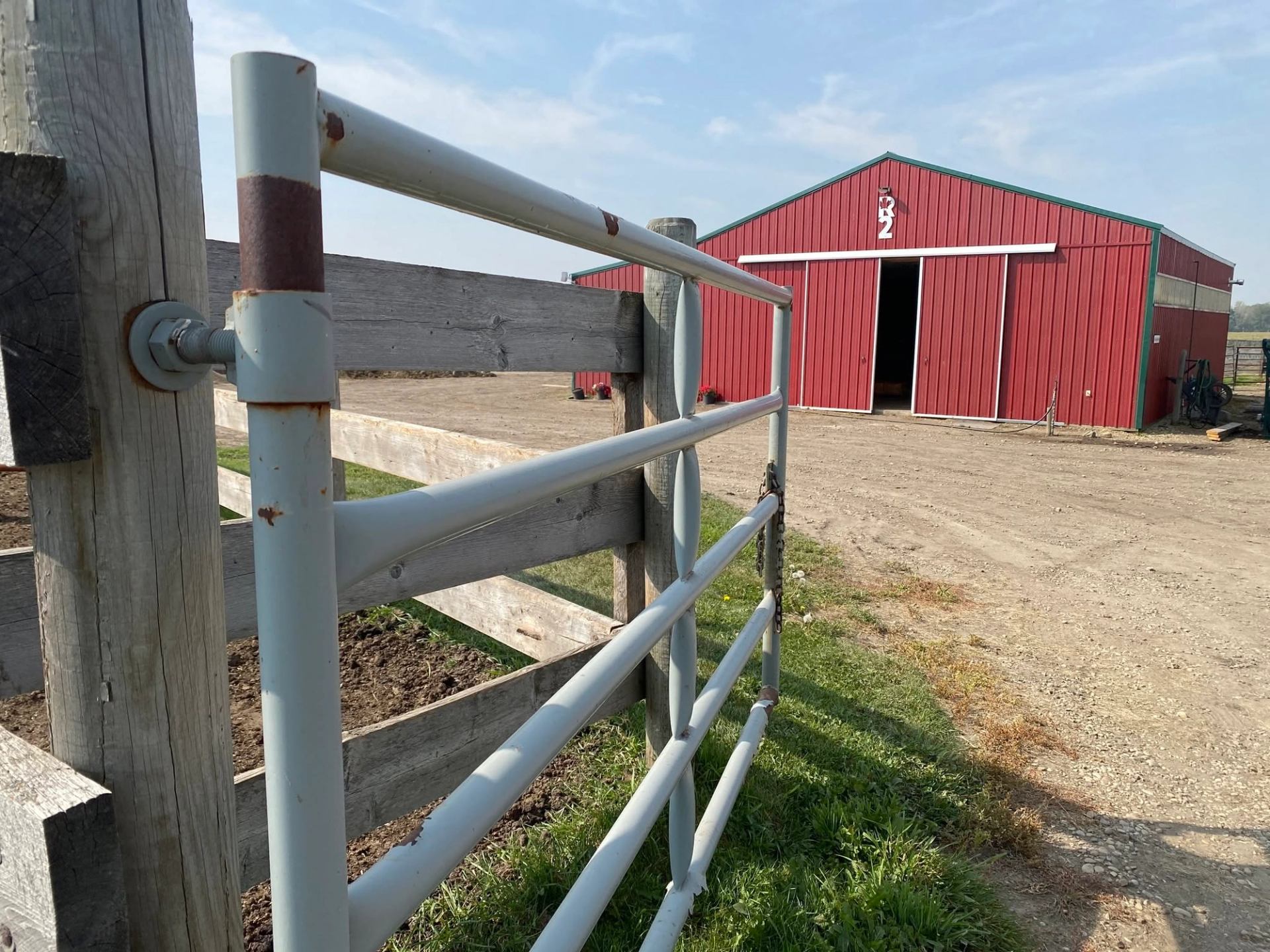 Metal farm gate and wooden fence leading toward a large red barn building.