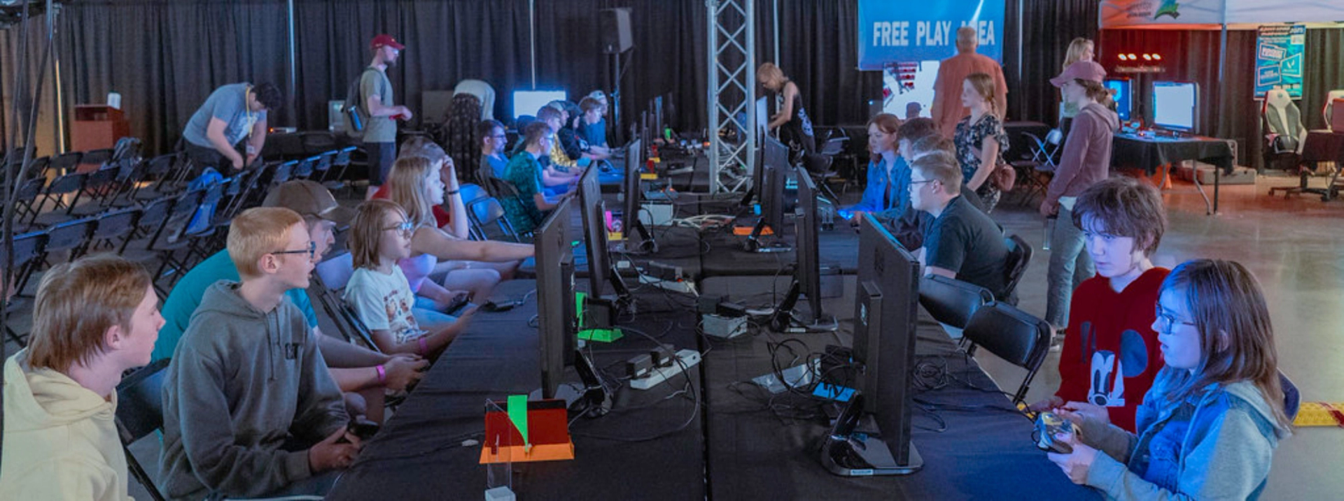 People playing video games at multiple monitors in a free play gaming area at a conference.
