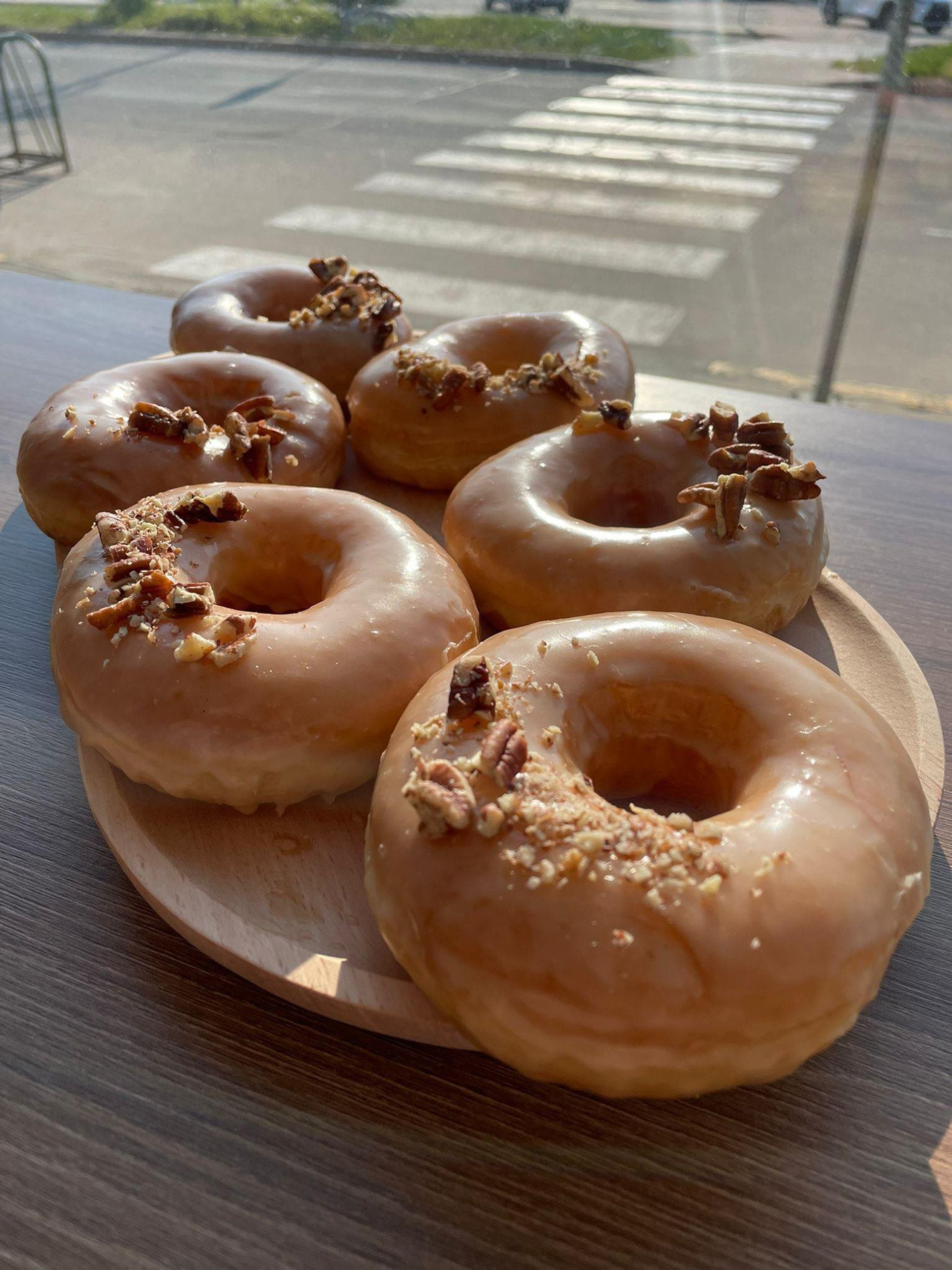 Plate of glazed donuts topped with bacon on wooden table near window.