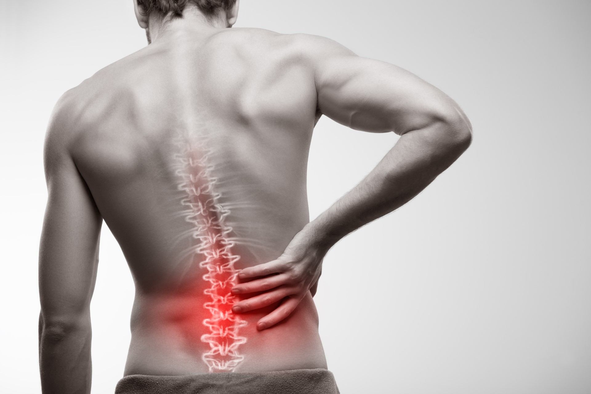 Person holding lower back with spine graphic and red highlight on lower spine.