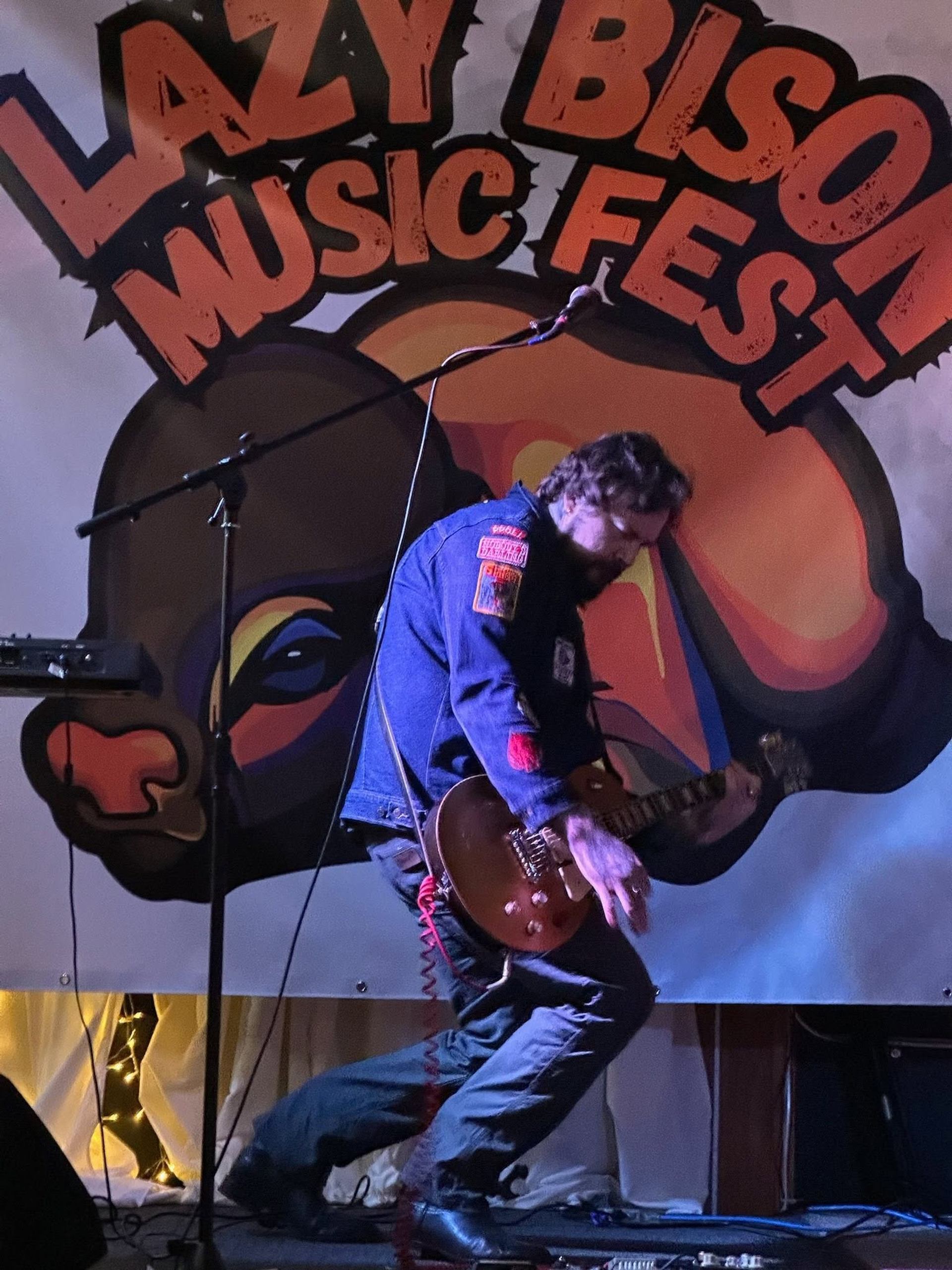 Guitarist performs beneath a Lazy Bison Music Fest sign.