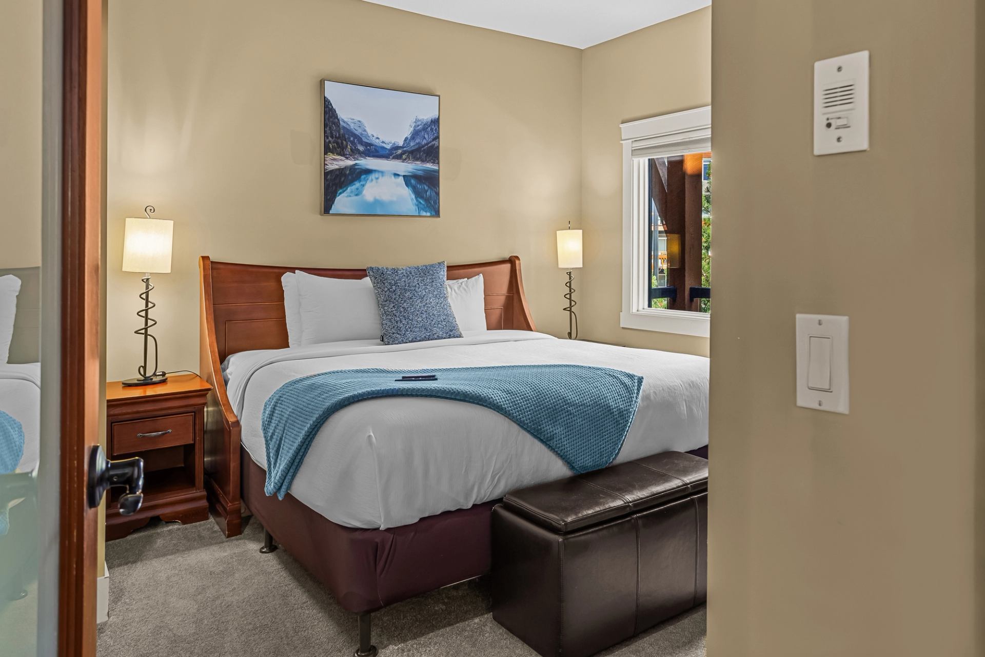 Bedroom with white bedding, blue throw, bedside lamps and leather bench.