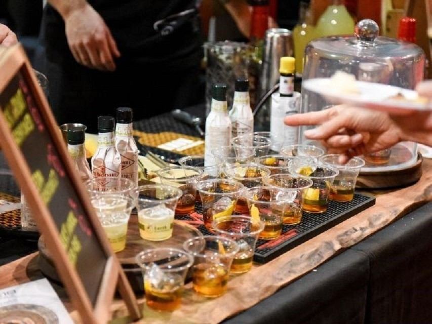 Table with small plastic cups of dark drinks and lemon slices at tasting event.