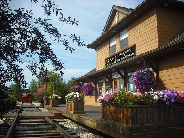 Historic-style visitor centre with flowers, white trim, and nearby railroad tracks.