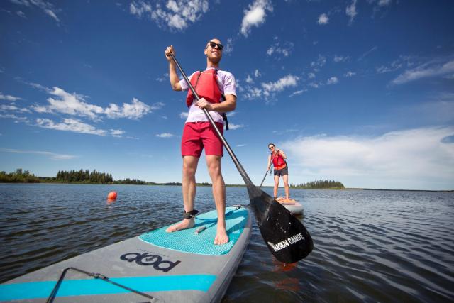 Couple stand-up paddle boarding on Astotin Lake in Elk Island National Park.