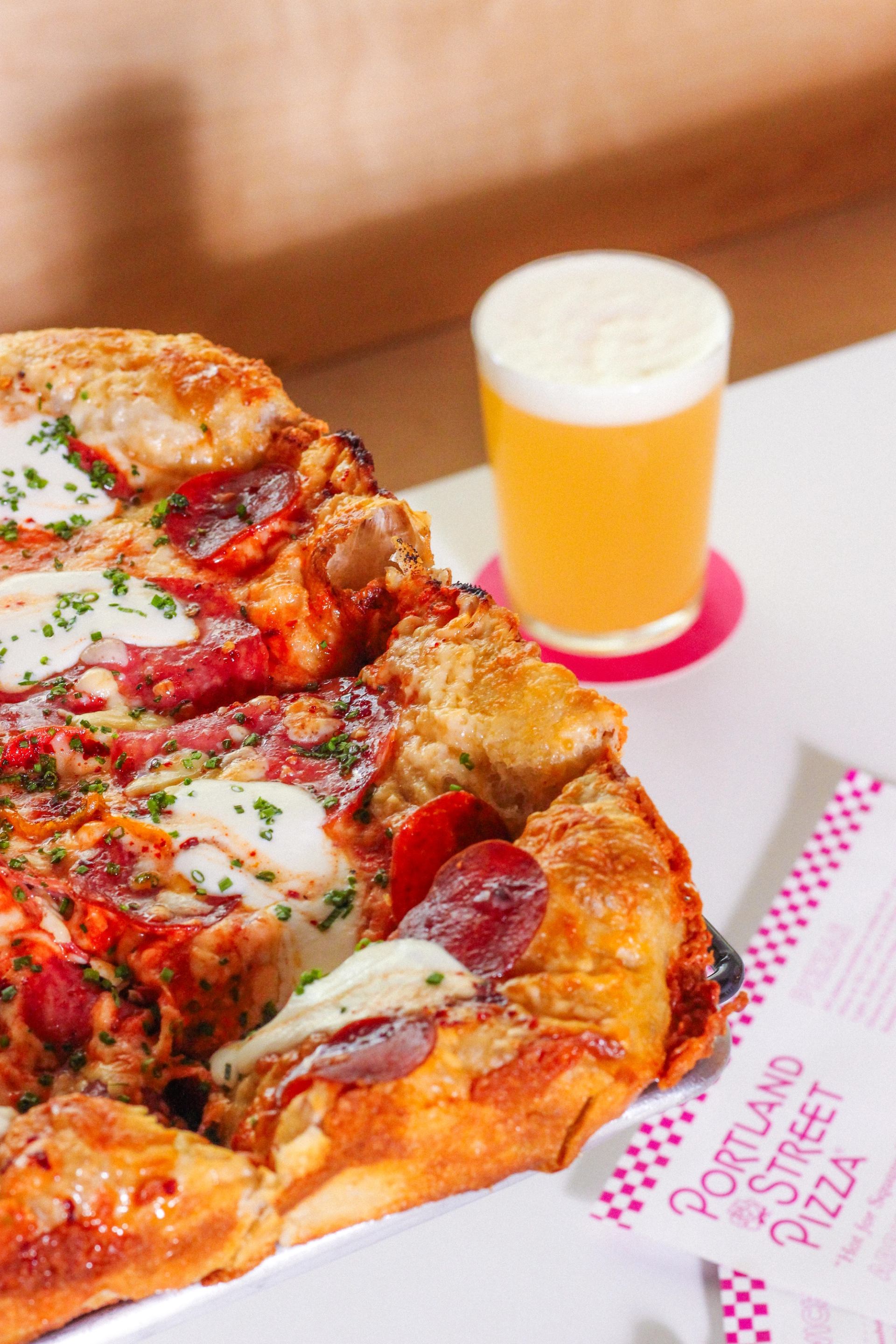 Close-up of cheesy pizza with a glass of craft beer on a white table.