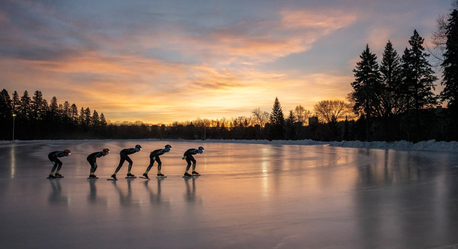 Silhouetted speed skaters circle the ice track at sunset in Victoria Park, Edmonton.