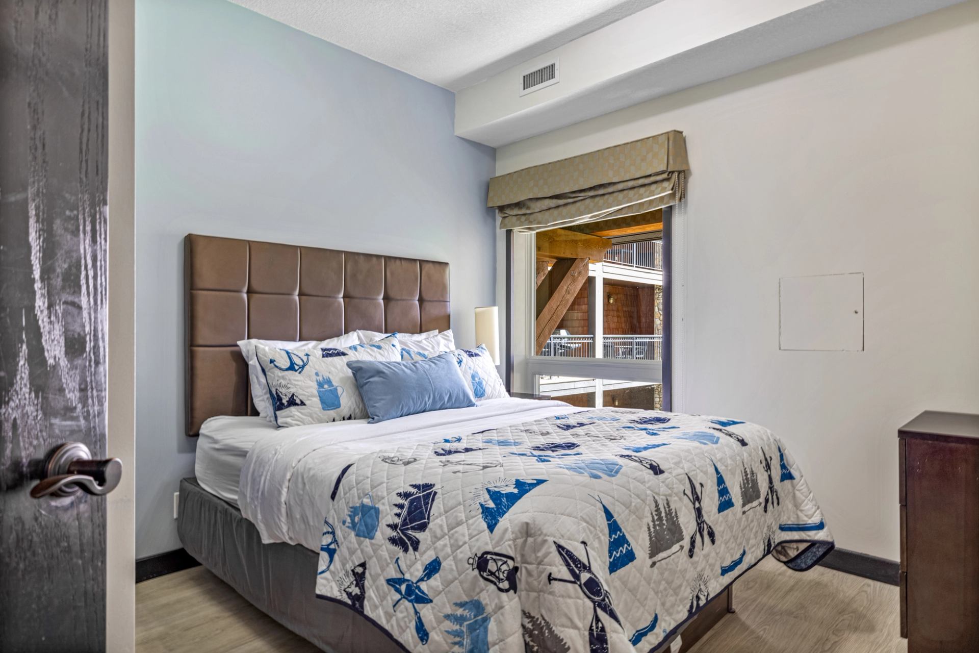 Bedroom with patterned bedding, padded headboard and a window overlooking wooden balconies.