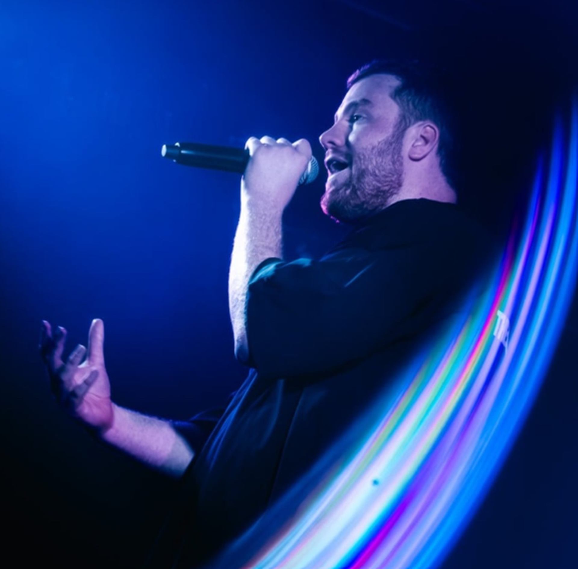 Singer holding a microphone on stage with blue and purple light streaks.