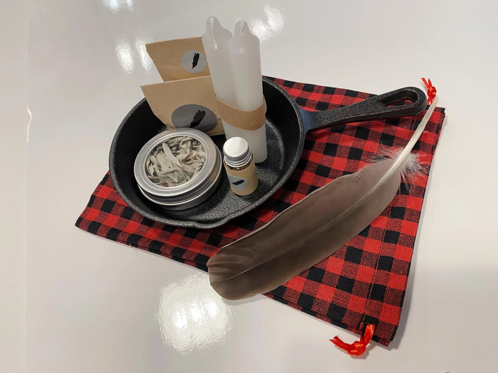 Gift tray with feather, ceramic jar, small bottle, and red-and-black checkered fabric mat.