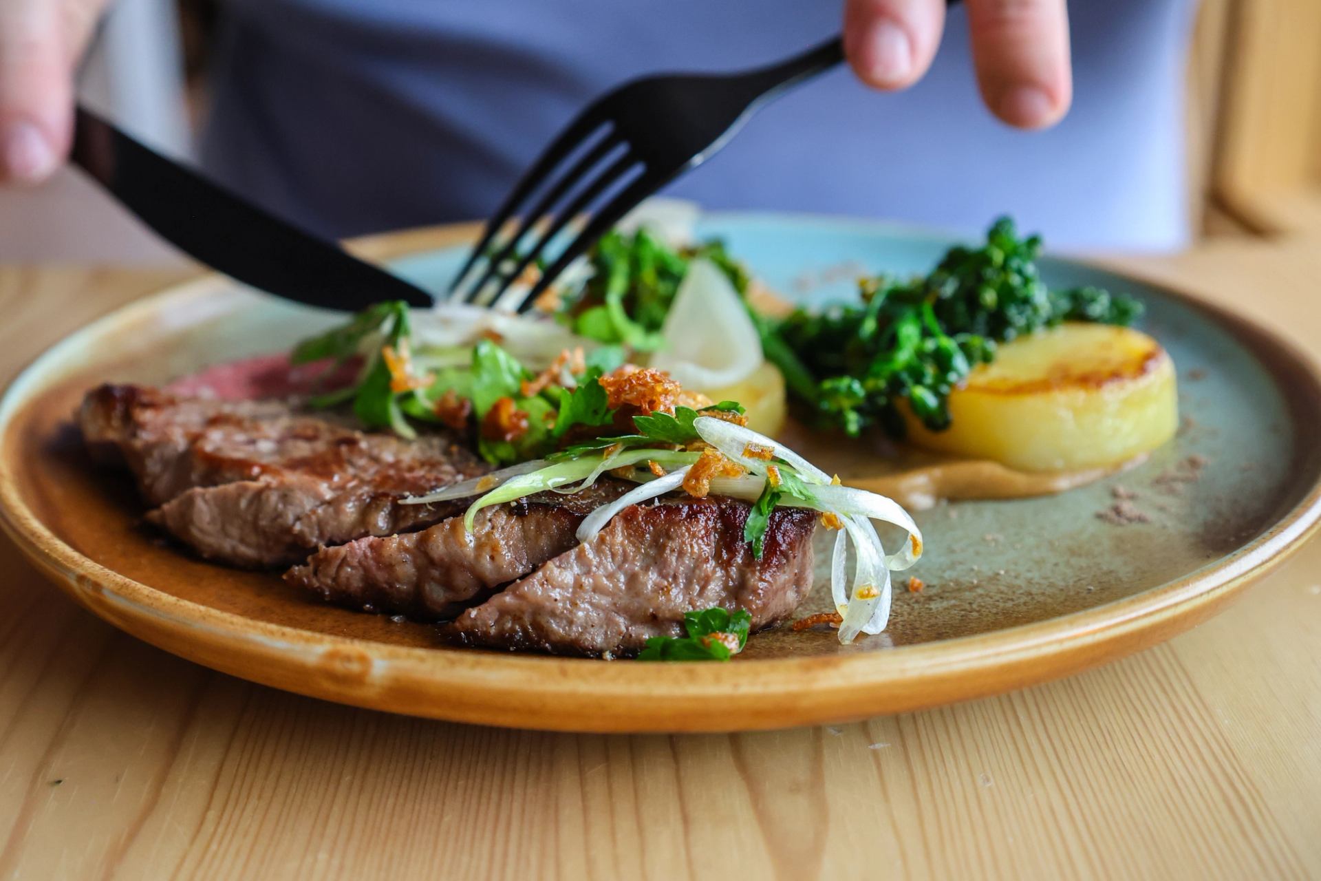 Grilled steak with greens and potato on a rustic plate, ready to be enjoyed.