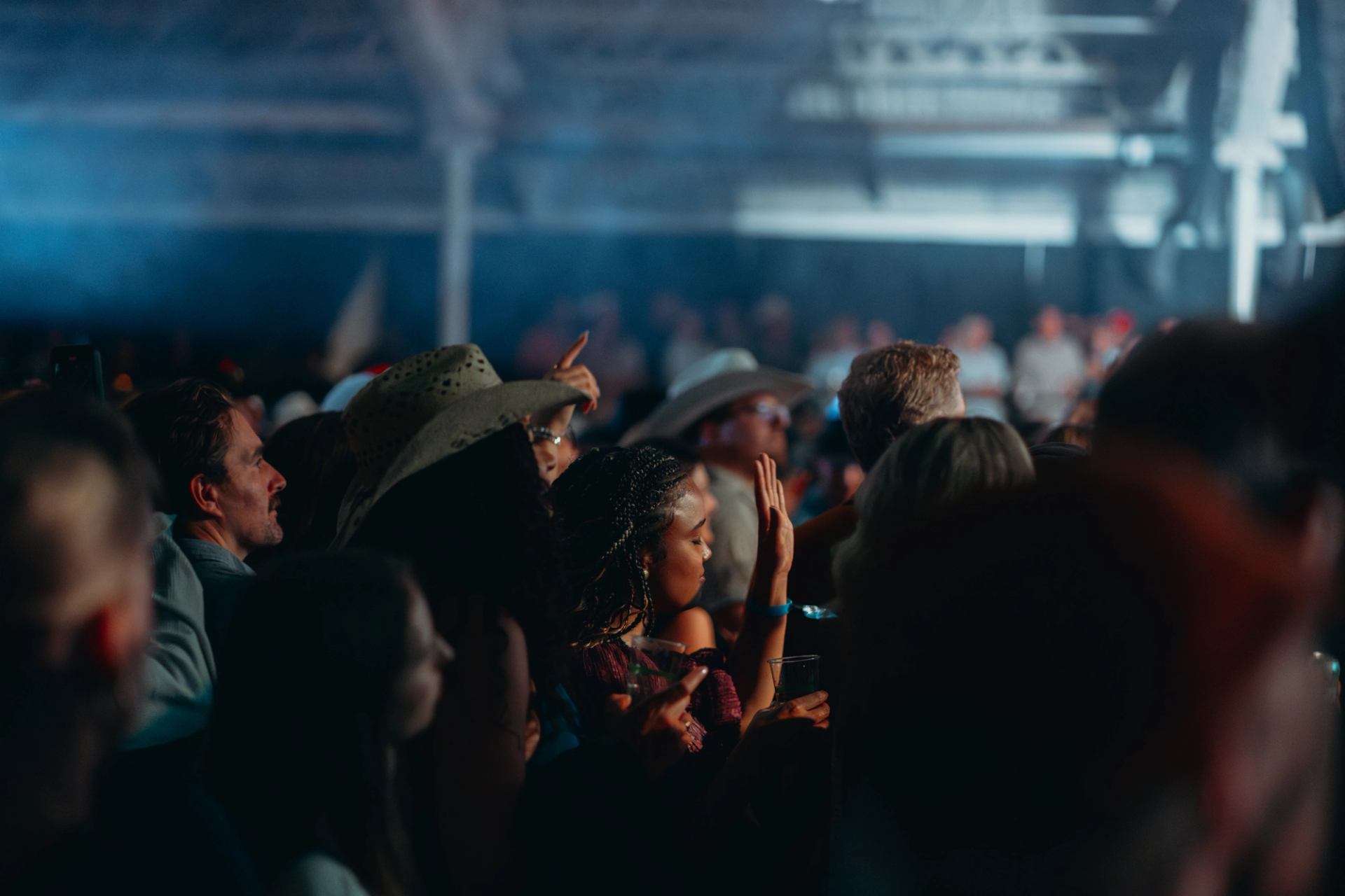 Concertgoers in cowboy hats watch the stage in a packed venue.