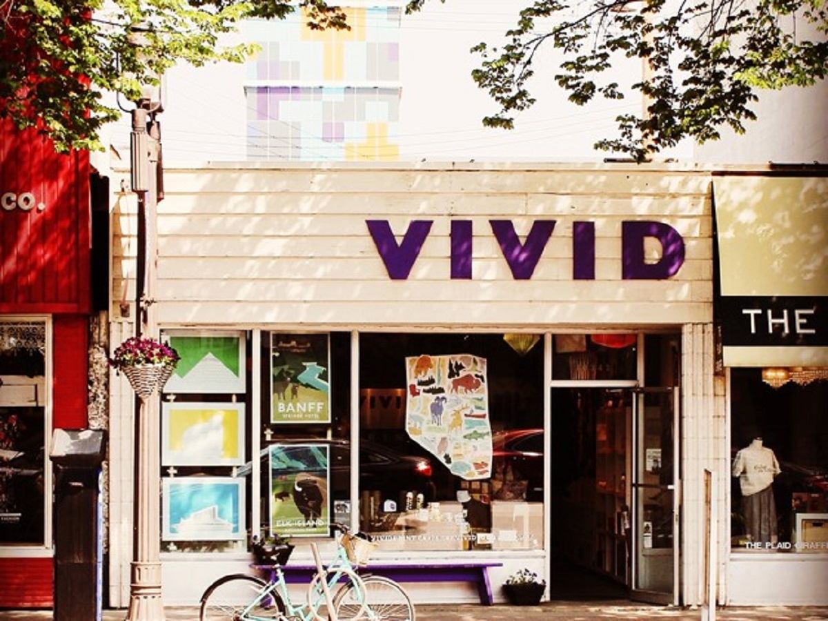 Storefront sign reading “VIVID” with posters in windows, outdoor bike and trees above.