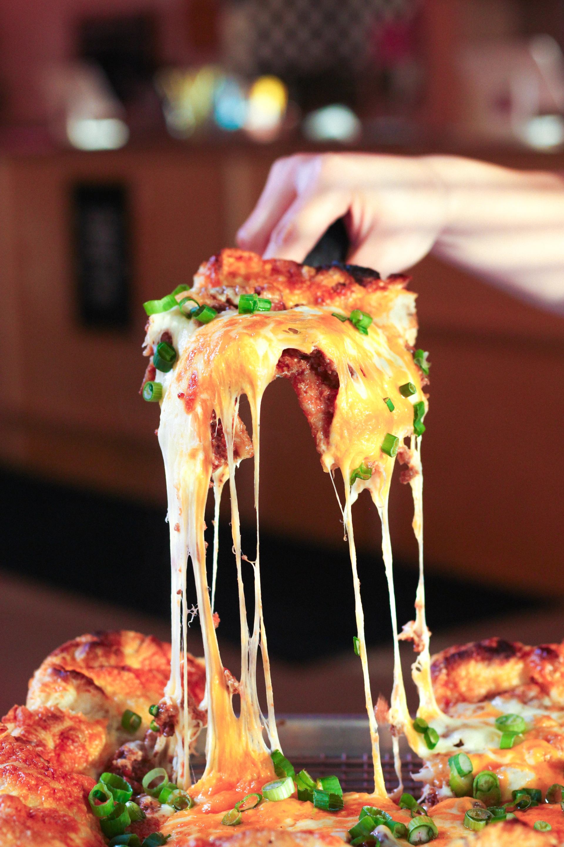 Cheesy pizza slice being lifted with gooey melted cheese stretching from the pie.